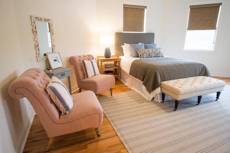 Large master bedroom featuring blush and navy accents throughout. A small seating area with oversized blush sitting chairs and pillows from Lulu & Georgia provide a perfect space to relax. A striped rug covers natural wood floors and accents the neutral colors in the bedding, as well.