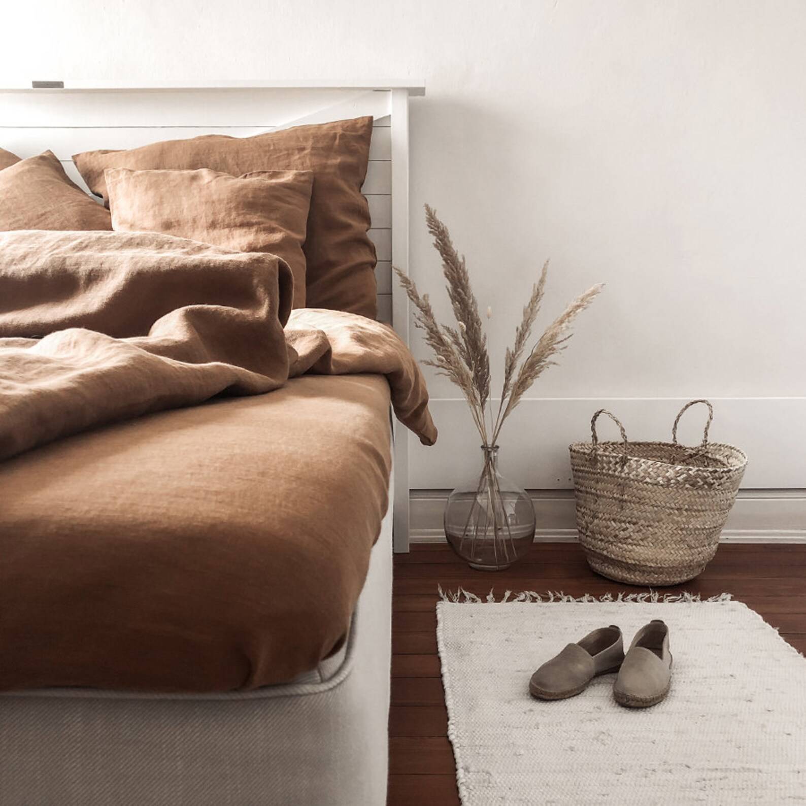 Linen bedding Liv cinnamon, bed linen with wooden buttons, duvet cover pillowcover, soft bedding stonewashed cinnamon brown white wall bedroom with white textured throw rug shoes on rug basked pampas grass in jug