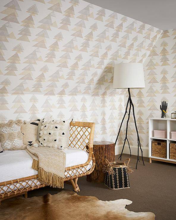 A Serena & Lily Avalon Daybed accented with boho chic pillows sits on a light brown cowhide rug against a wall clad in tan and gray geometric wallpaper. The bed is placed beside a tree trunk accent table and lit by a black faux bois floor lamp.