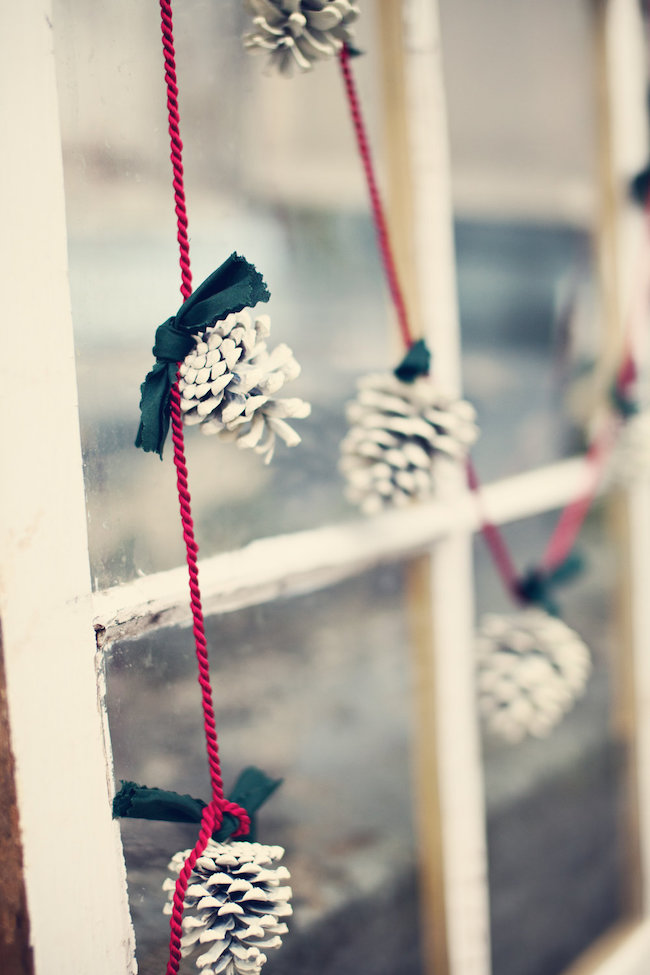 Frosted pinecone garland with green ribbon and red rope hung on window.