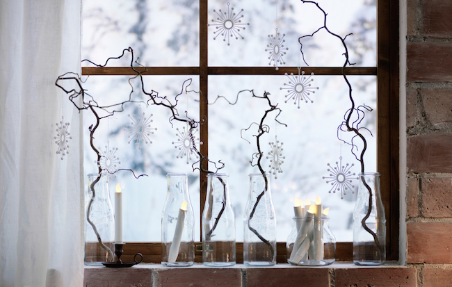 Glass bottles with branches and snowflakes decorations on window.