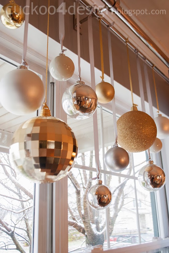 Silver and gold glass ball ornaments hung from matching ribbon in window.
