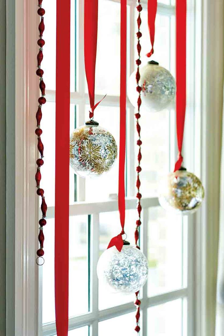 Silver and gold glass ball ornaments hung from red ribbon in a window.