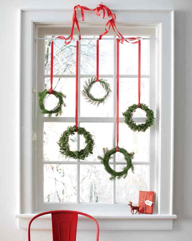 Tiny wreaths hung with red ribbon on a window.
