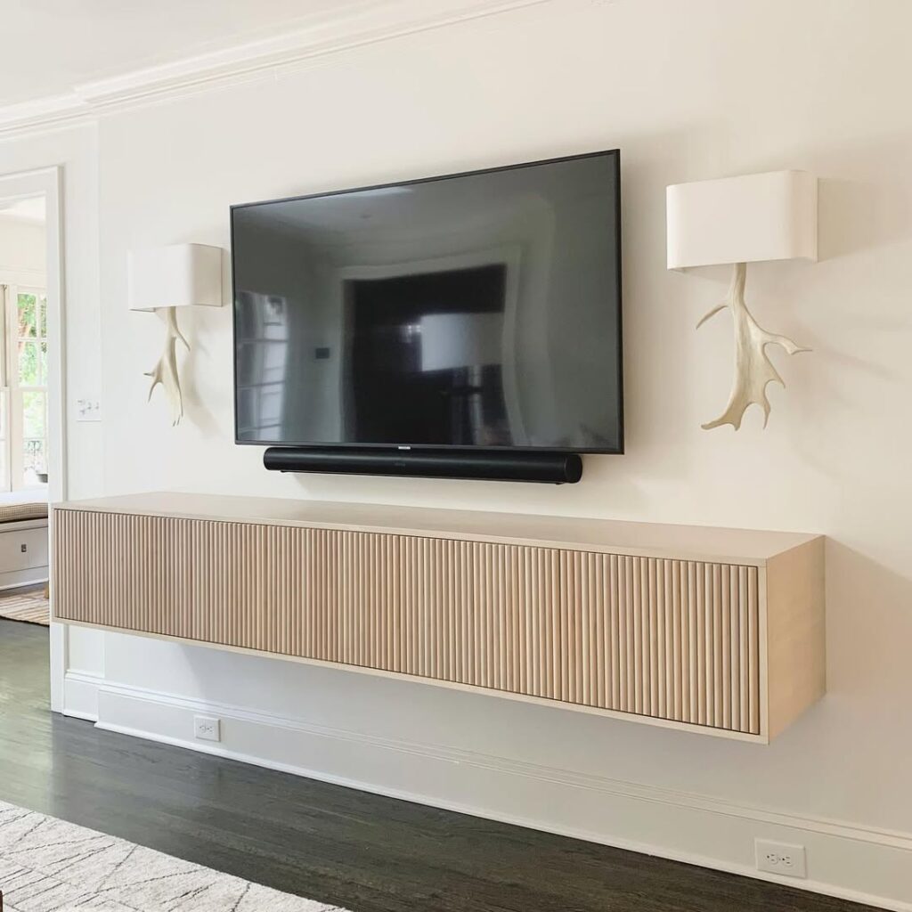 Light oak floating slatted stand with warm antler sconces flanking TV wall