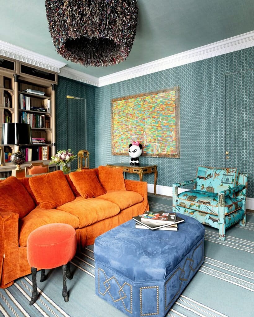 The walls are patterned teal beside a pumpkin velvet sofa